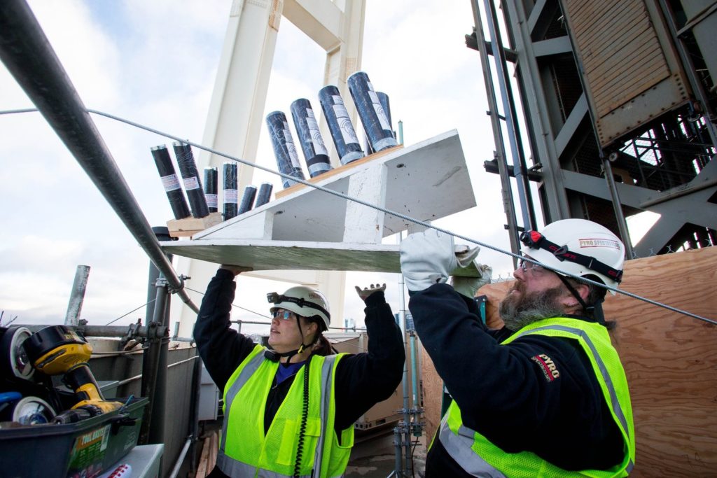 Heidi Kirk, left, and Kevin Underwood from Pyro Spectaculars lift fireworks over the railing on the SkyLine level of the Space Needle. (Courtney Pedroza/The Seattle Times)