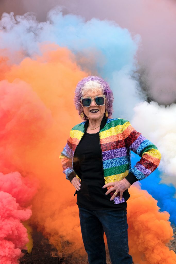 Judy Chicago Stands in her rainbow smoke art